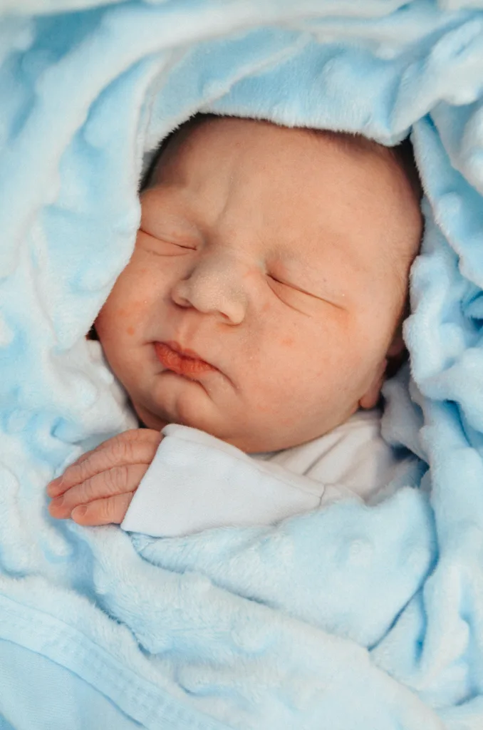 A serene photo captures a sleeping newborn in Cleethorpes, wrapped snugly in a soft, fluffy light blue blanket. The baby's peaceful expression and delicate fingers peeking out create an atmosphere of gentle tranquility. © Aimee Lince Photography - Wedding photographer in Lincolnshire, Yorkshire & Nottinghamshire