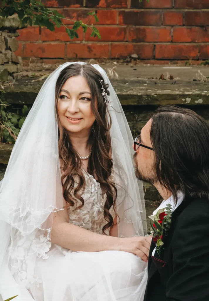 Lynsey and Jamie, a bride and groom, sitting on steps in a garden for their wedding photoshoot.