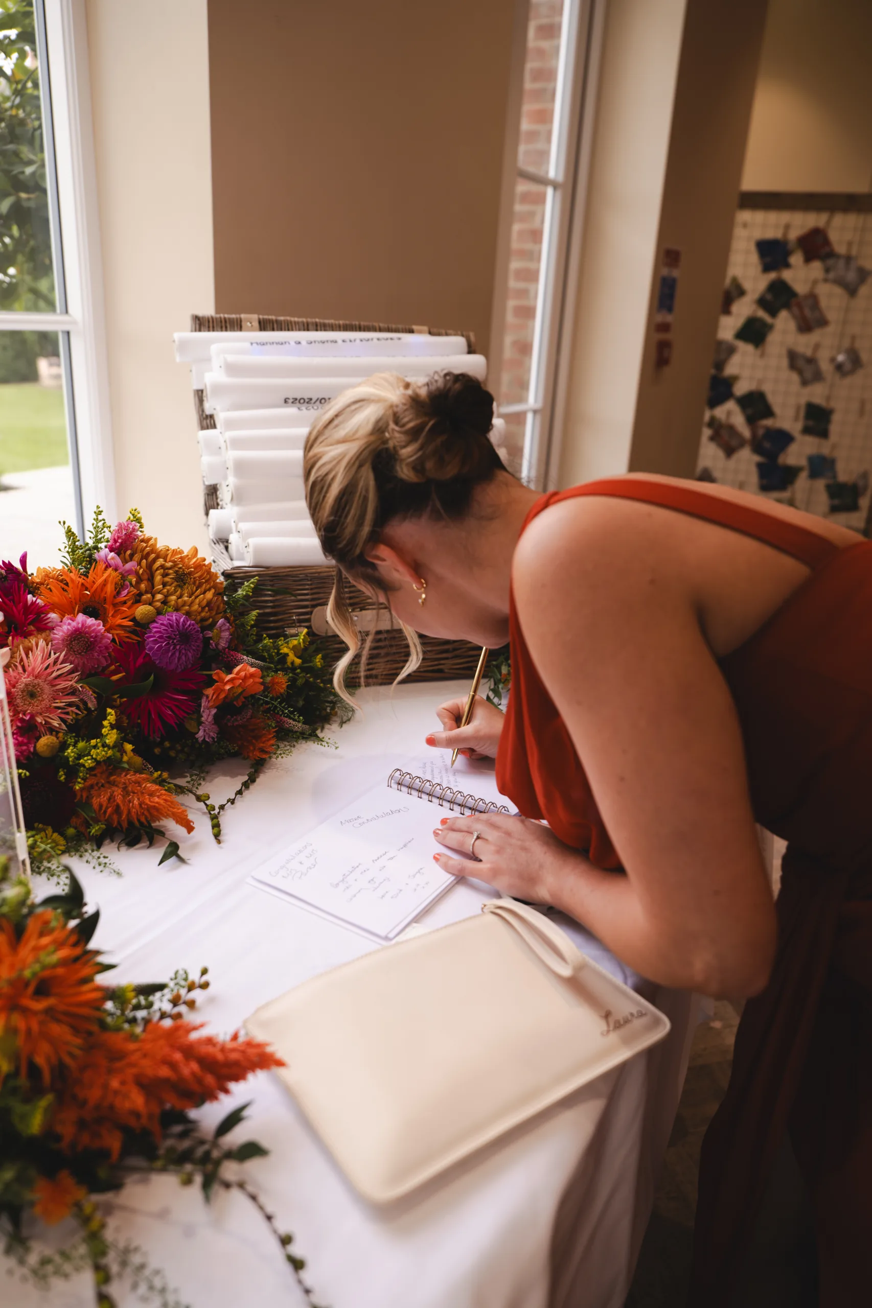 A bride signing her wedding guestbook at a table with flowers.