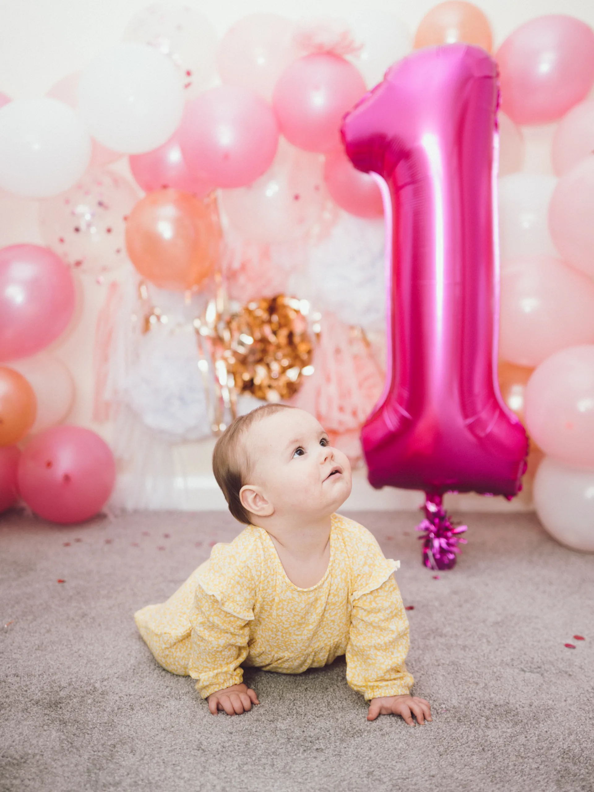 A baby girl is sitting in front of balloons for her first birthday photography.