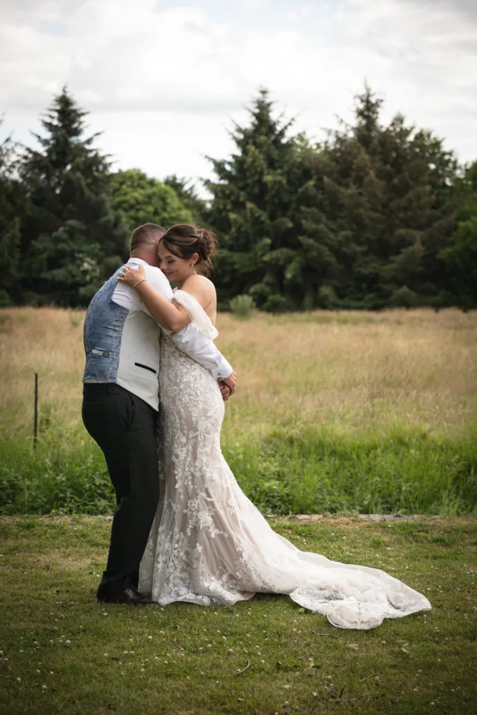 A bride and groom hugging in a field during their woodland wedding.