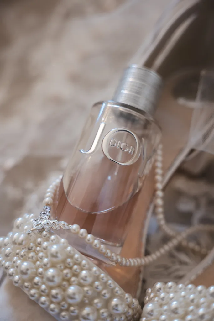 A bottle of perfume and a pair of shoes on a bed for a woodland wedding.