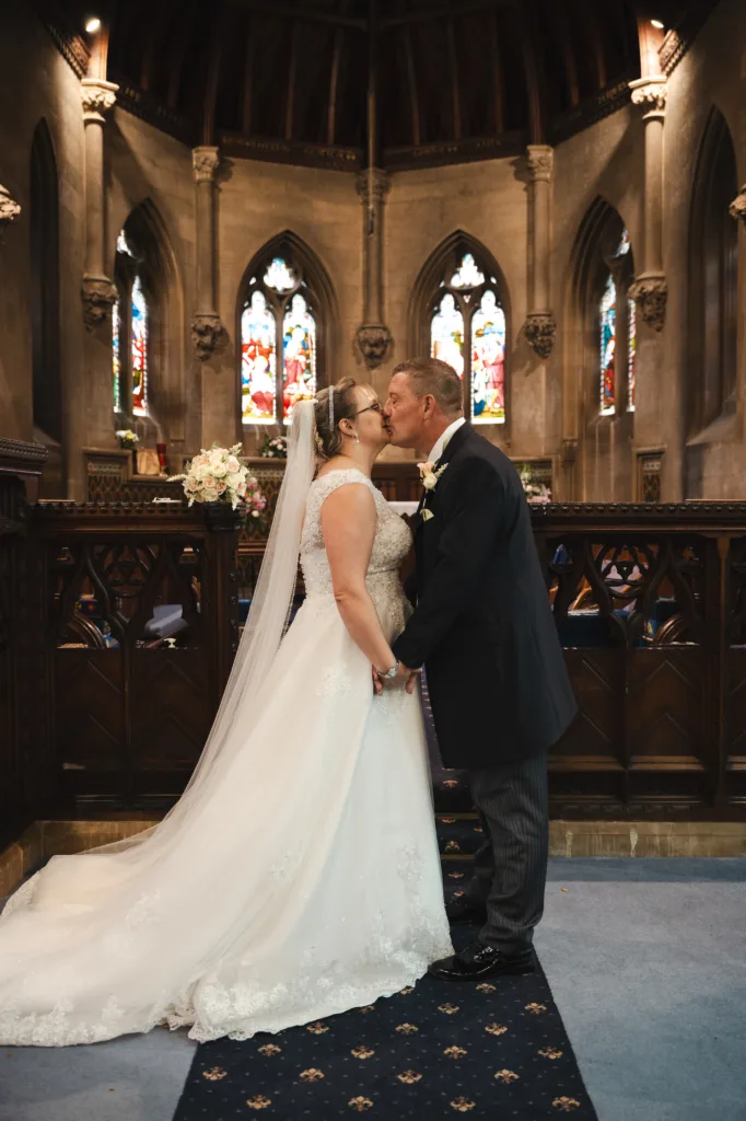 A bride and groom sharing a romantic kiss in a church after exchanging wedding vows during their rainy wedding at Sleaford.