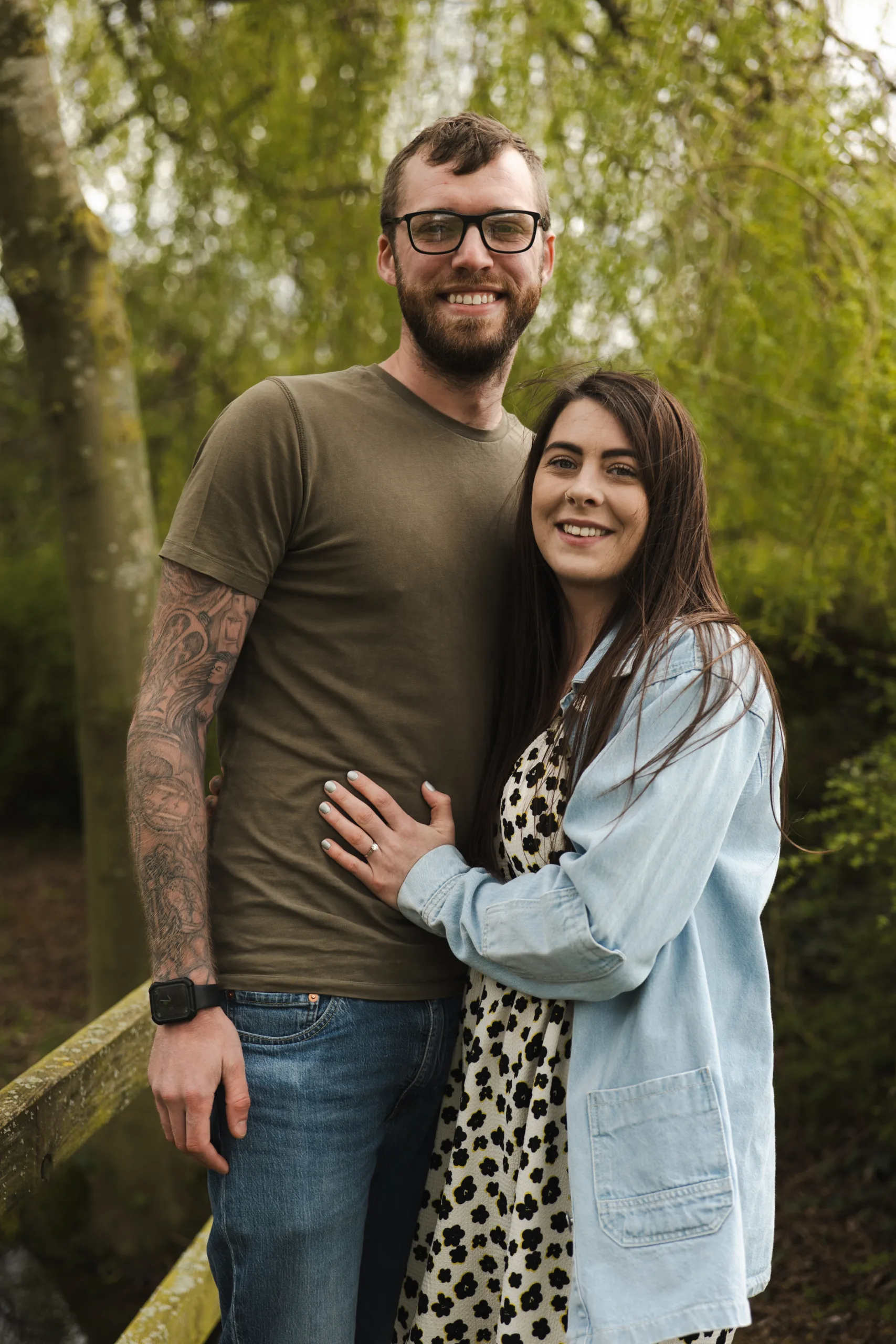 A couple posing for an engagement photo in a wooded area at Hall Farm Hotel.