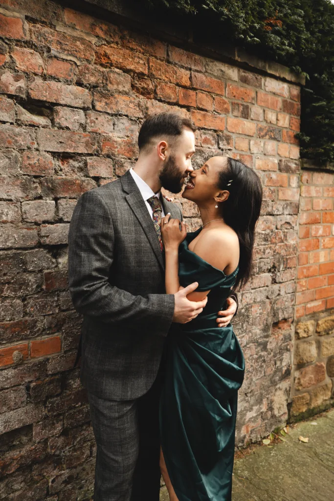 A couple engaged in an intimate kiss against a brick wall, capturing the essence of their Lincoln engagement session with street photography flair.