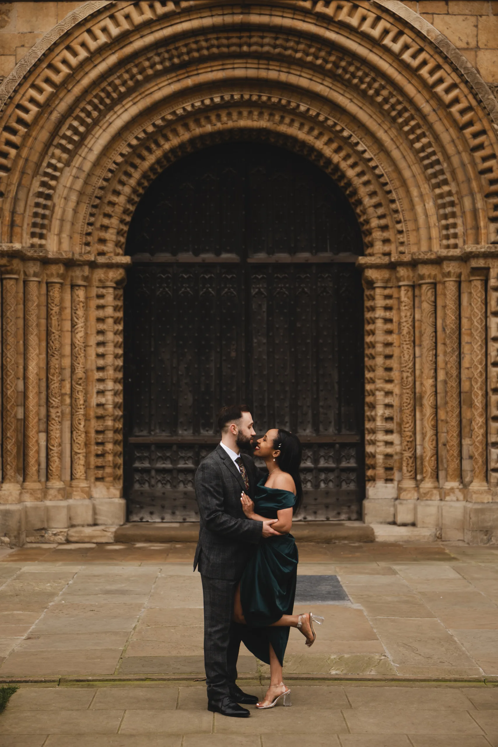 An engaged couple kissing in front of Lincoln Cathedral during their engagement session.