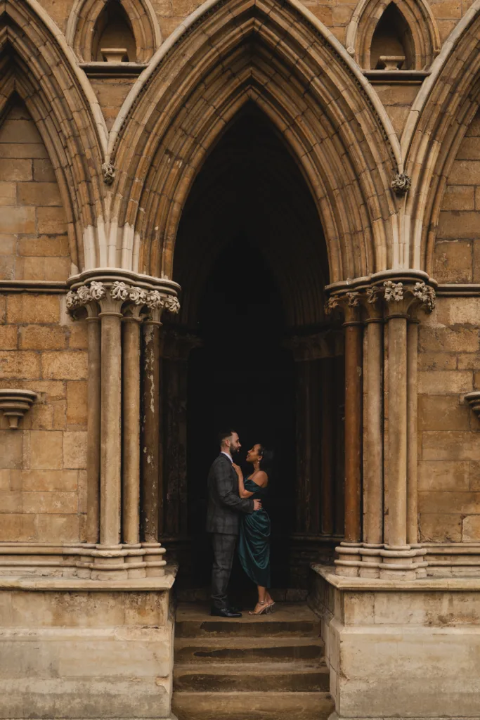 A bride and groom standing in front of an ornate building during their engagement session.