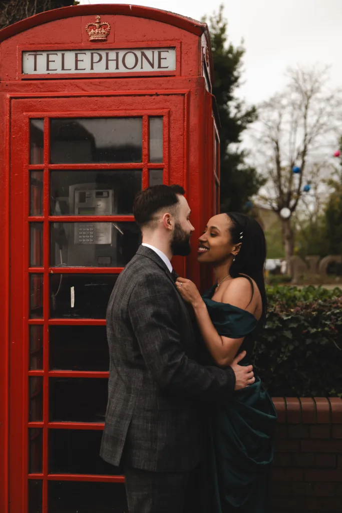 A couple engaged in a passionate kiss in front of a red telephone booth during their engagement session. The street photography captures this romantic moment beautifully.