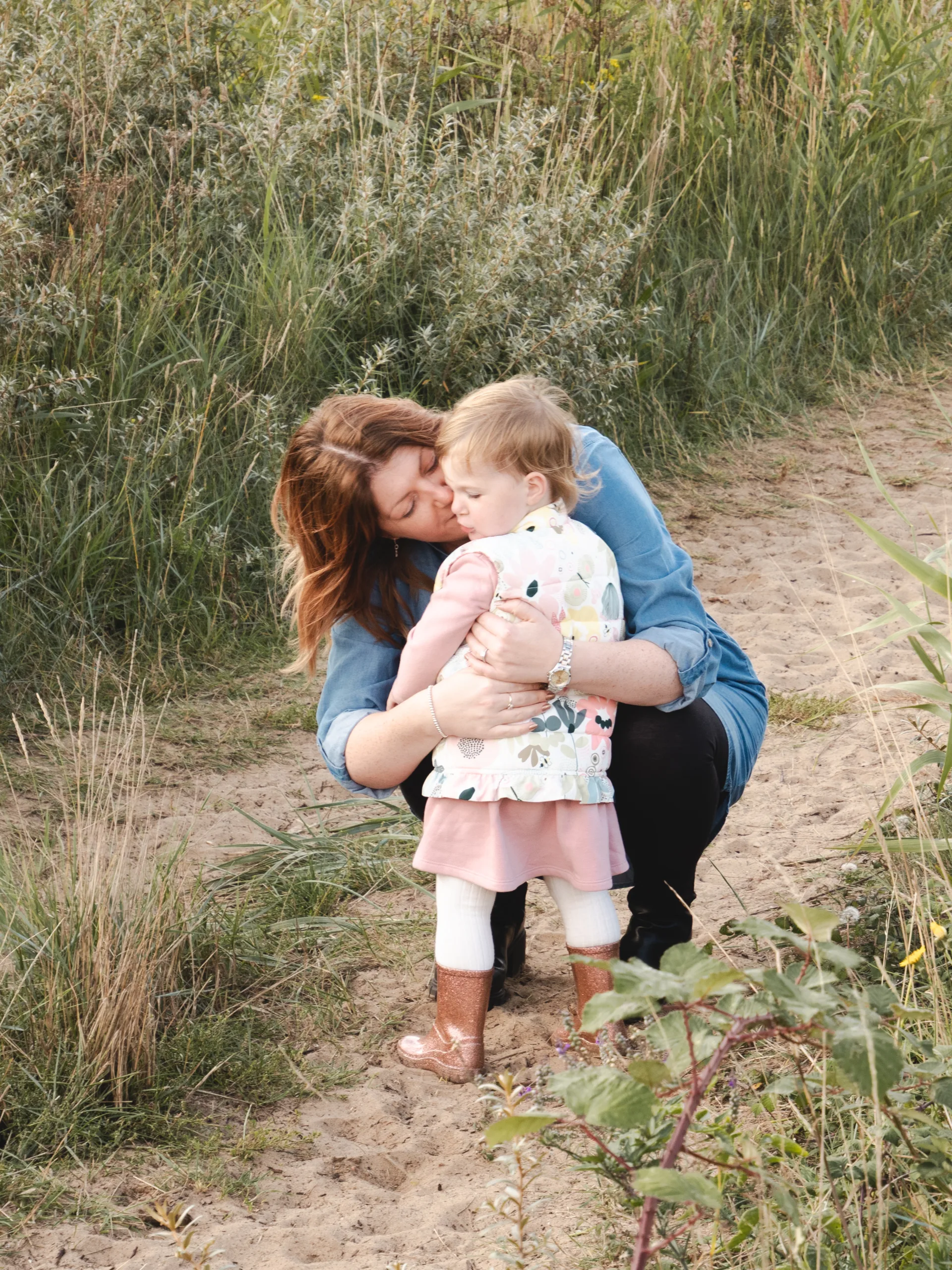 A heartwarming family moment captured in a photography of a woman hugging a little girl on a dirt path.