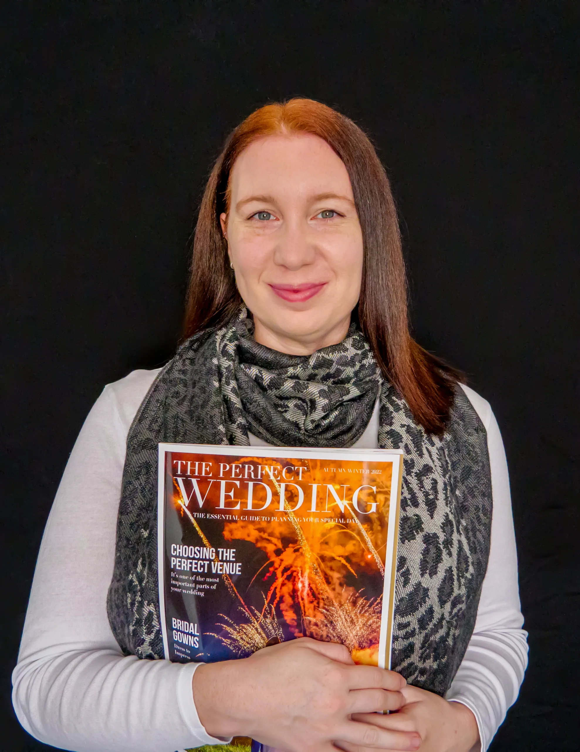 A woman holding a published copy of The Perfect Wedding magazine with a black background.