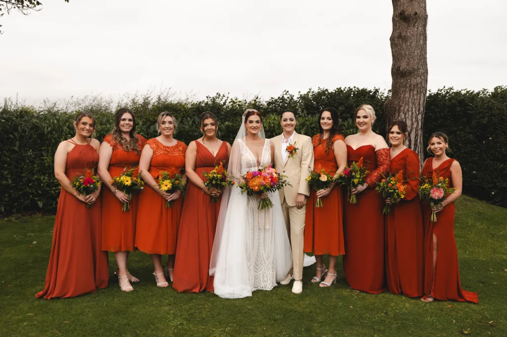 Two brides with a large group of bridesmaids in orange dresses at an autumn themed wedding, posing for a photo at Stallingborough Grange.