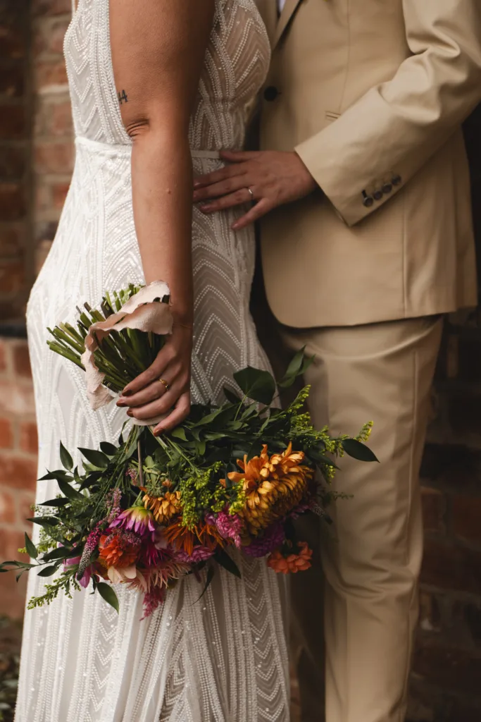 An autumn-themed wedding ceremony at Stallingborough Grange, captured beautifully with the brides holding bouquets in front of a brick wall.