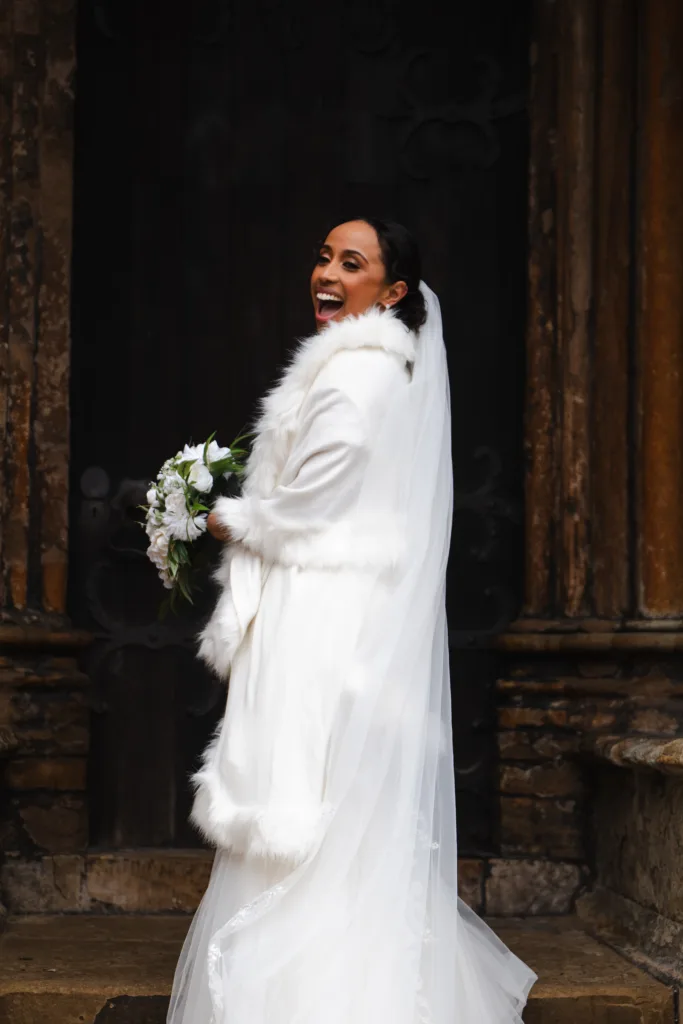 A bride in a white wedding dress laughing in front of the Lincoln Cathedral door.