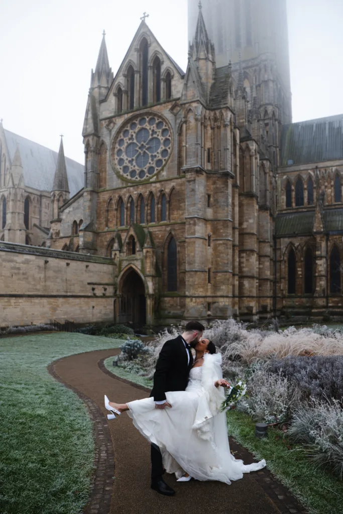 A bride and groom kiss in front of Lincoln Cathedral.