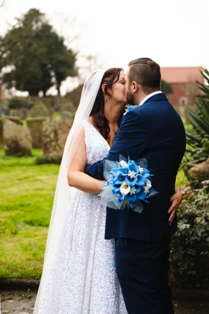 A festive bride and groom sharing a passionate kiss in the churchyard of East Drayton on their wedding day