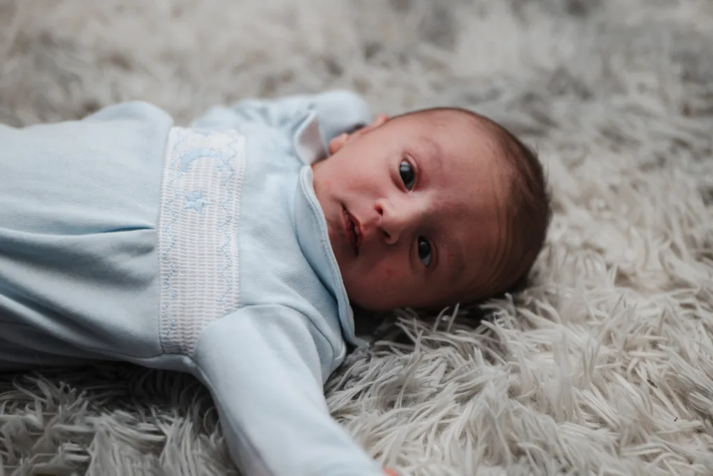A newborn is laying on a rug with a blue outfit.
