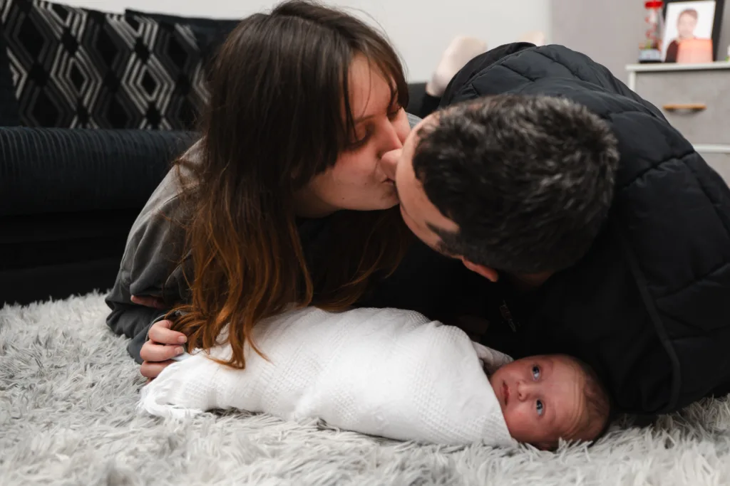 A couple tenderly kissing their newborn baby.