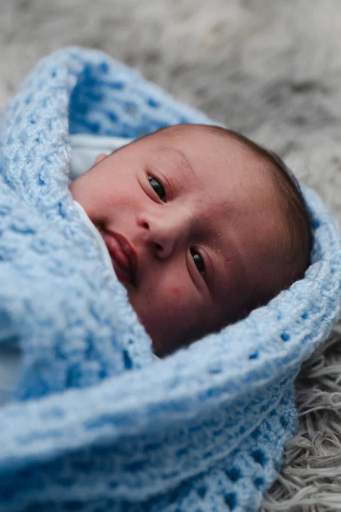 A newborn baby peacefully swaddled in a blue blanket.