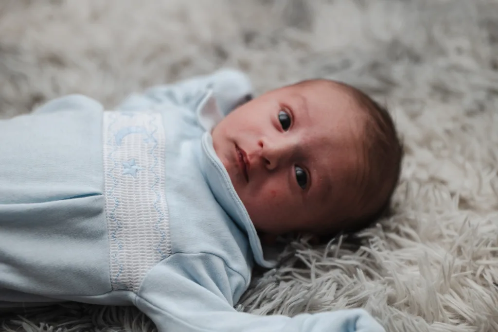 A newborn baby boy laying on a fluffy rug.