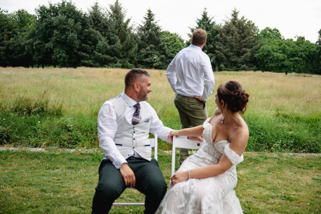 A bride and groom posing for a photo in chairs in a field.