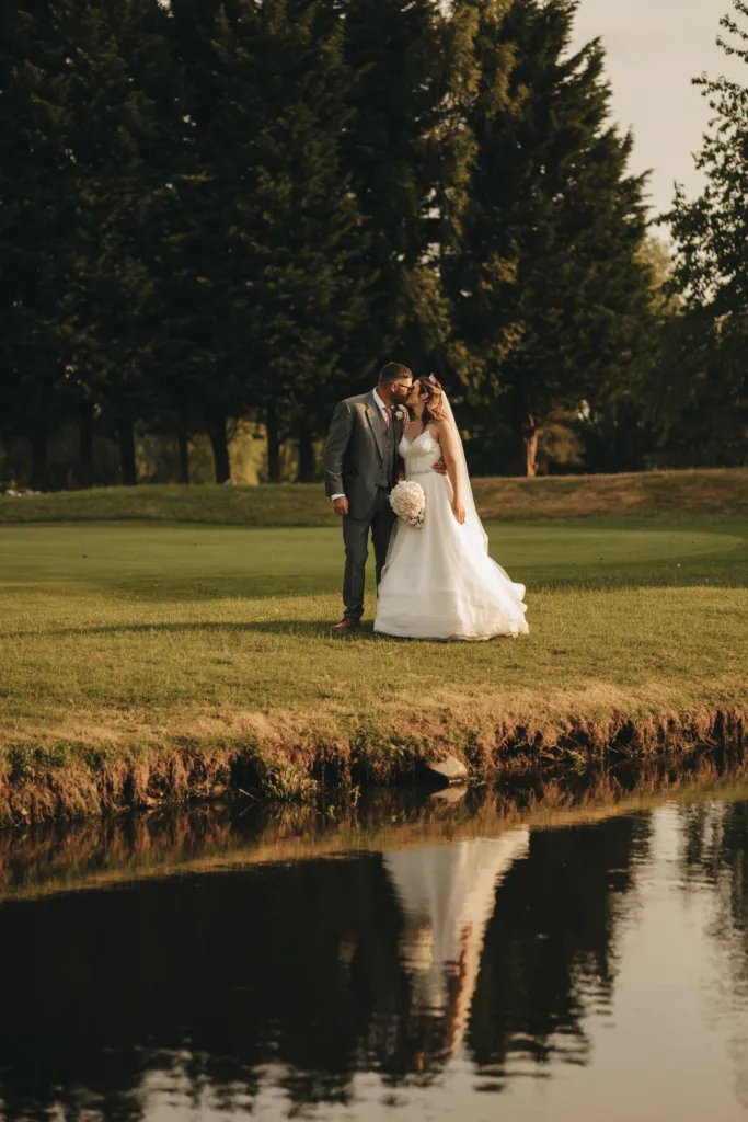 A bride and groom standing in front of a pond in Lincolnshire, captured by a photographer.