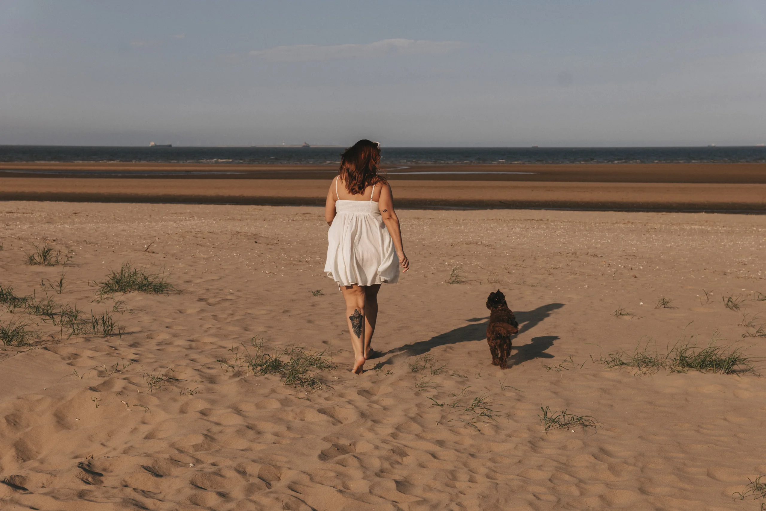 A woman walking her dog on the beach in Yorkshire.