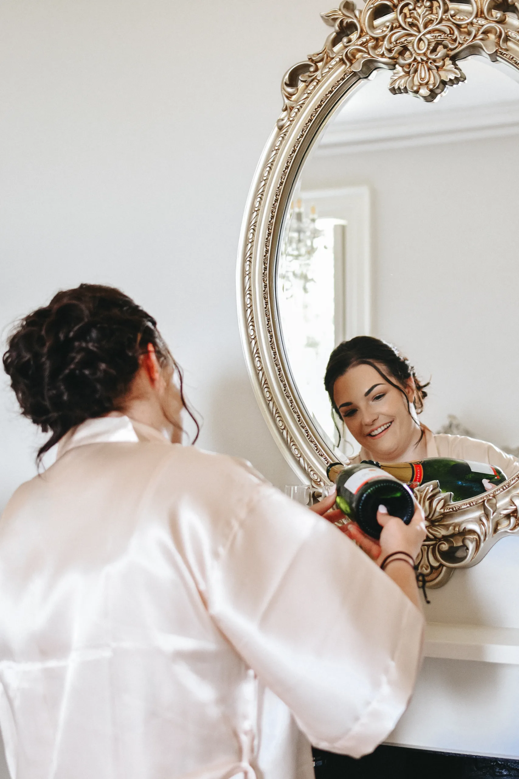 A bride getting ready for her wedding in front of a mirror while a photographer captures the moment.
