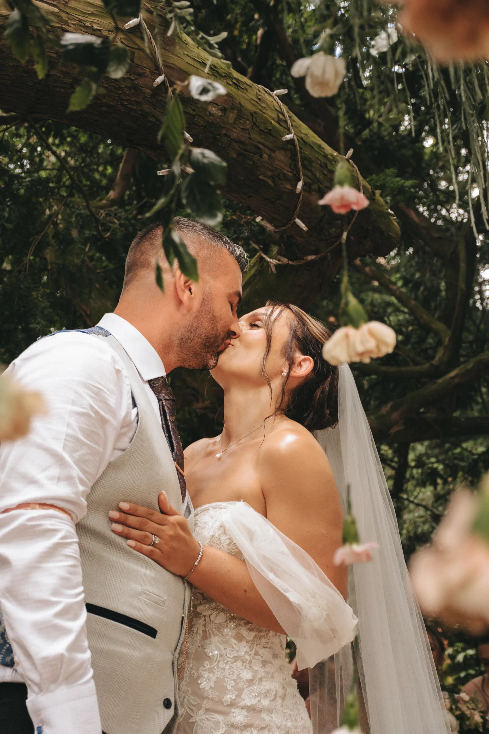 A bride and groom kiss under a tree in a Lincolnshire garden.