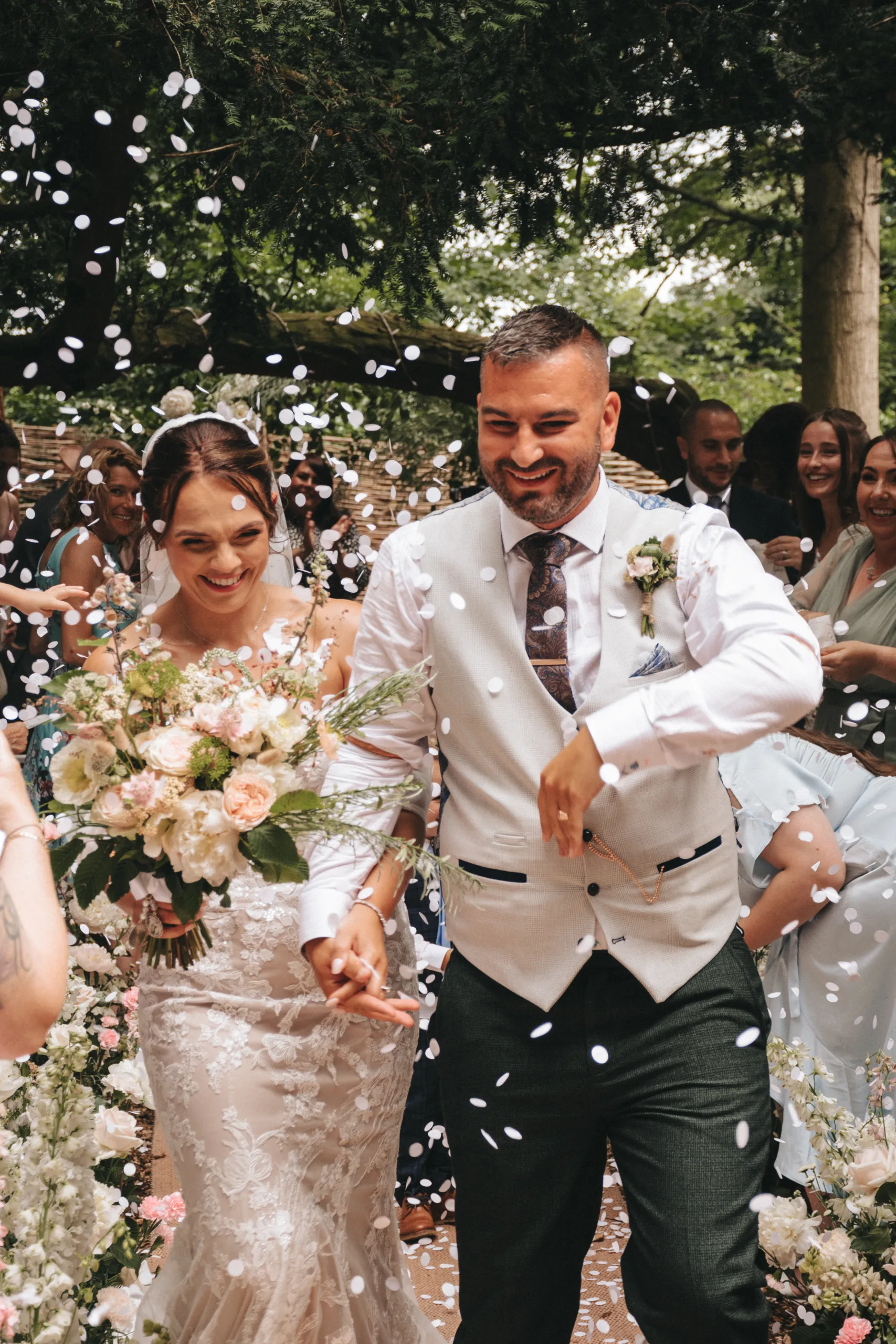 A bride and groom walk down the aisle in Yorkshire with confetti thrown at them, capturing the moment with photography.
