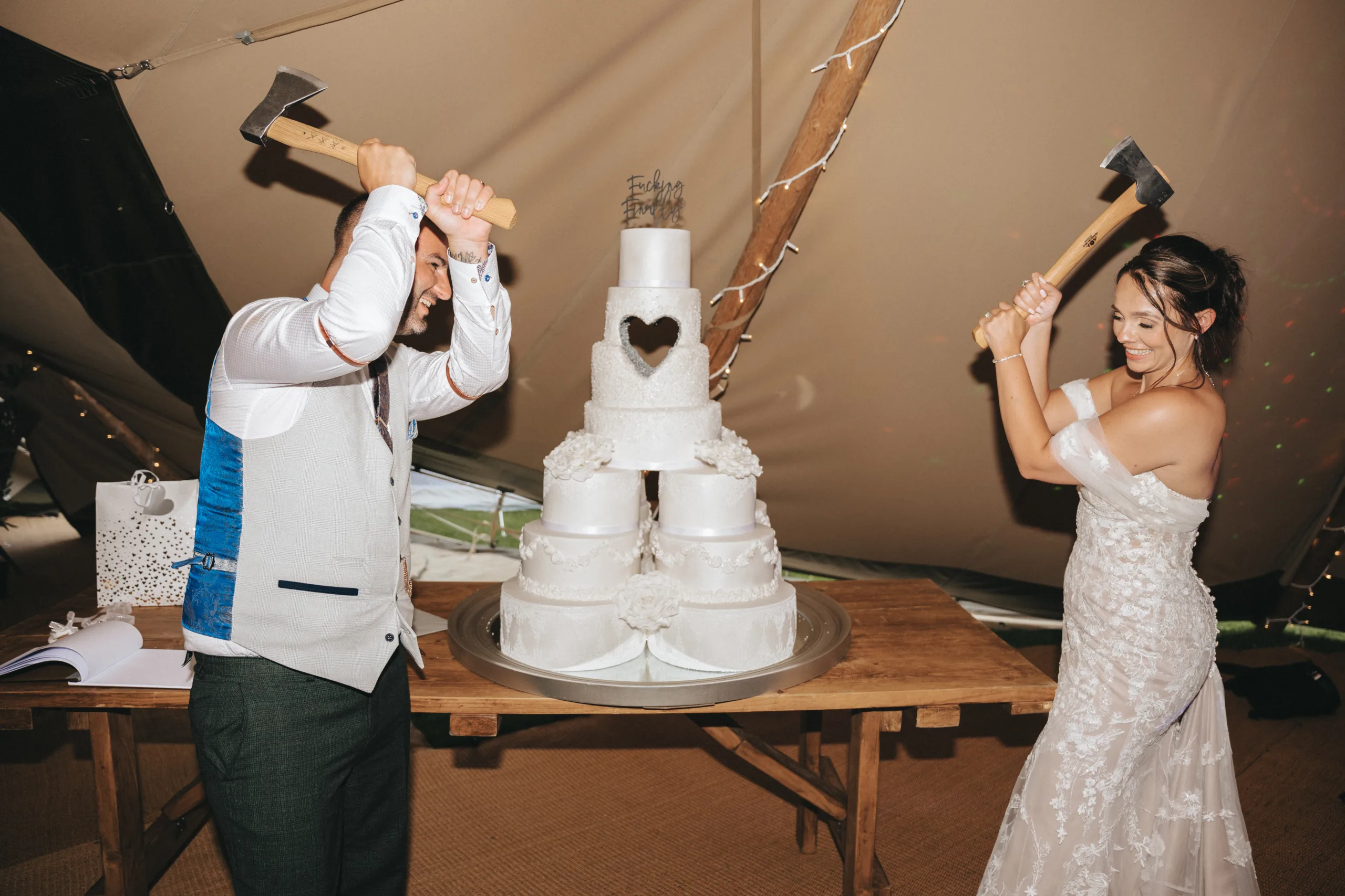 A bride and groom cutting their wedding cake with a hammer while a photographer captures the moment.