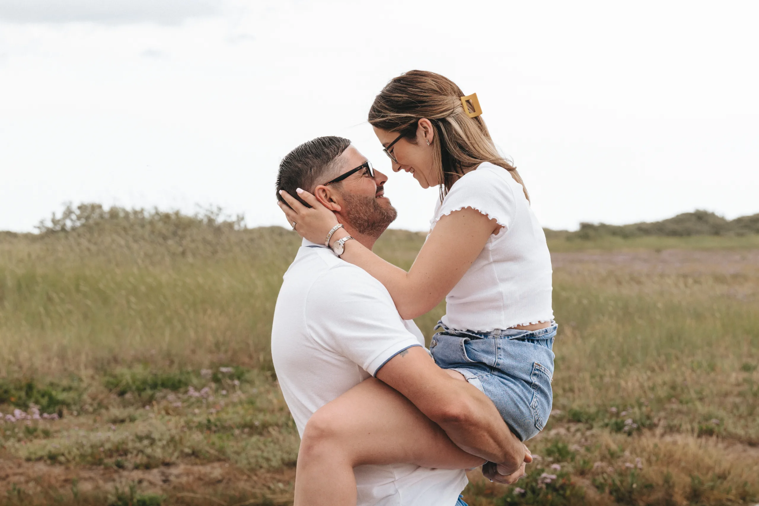 A man and woman embracing in a field, captured by a photographer.