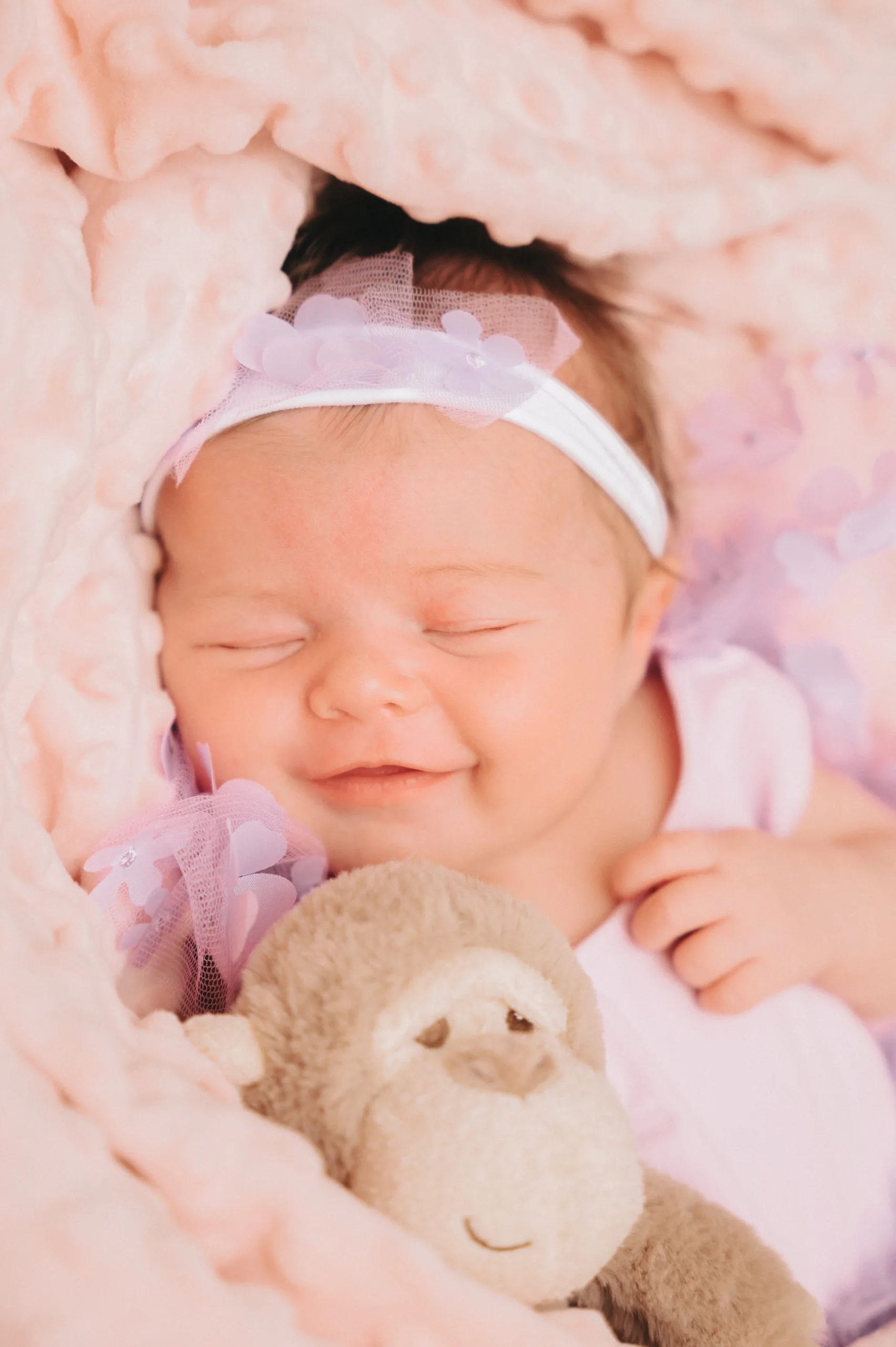 A baby girl is peacefully sleeping on a pink blanket with a teddy bear in Yorkshire.