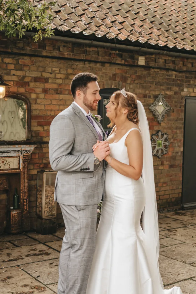 A bride and groom standing in front of a Yorkshire brick building, captured beautifully by wedding photography.