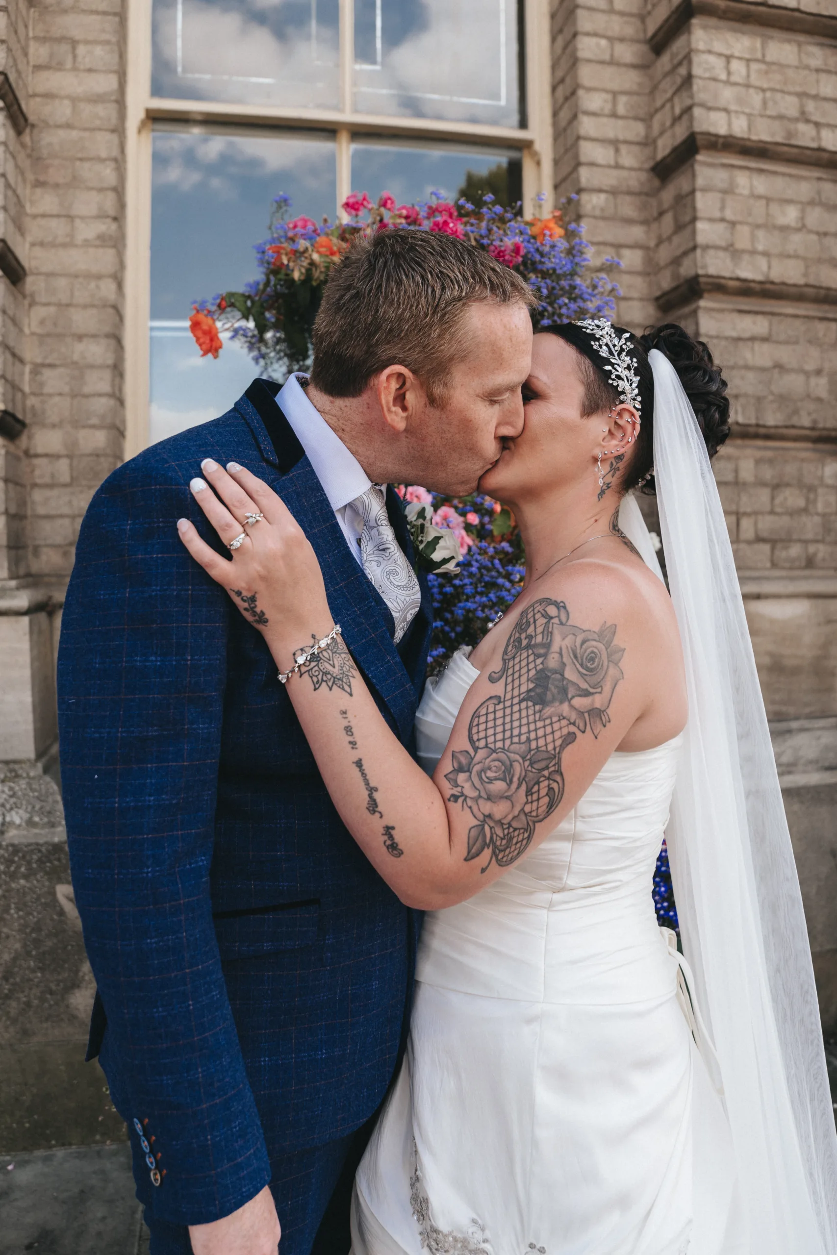 A bride and groom kissing in front of a building captured by a photographer.