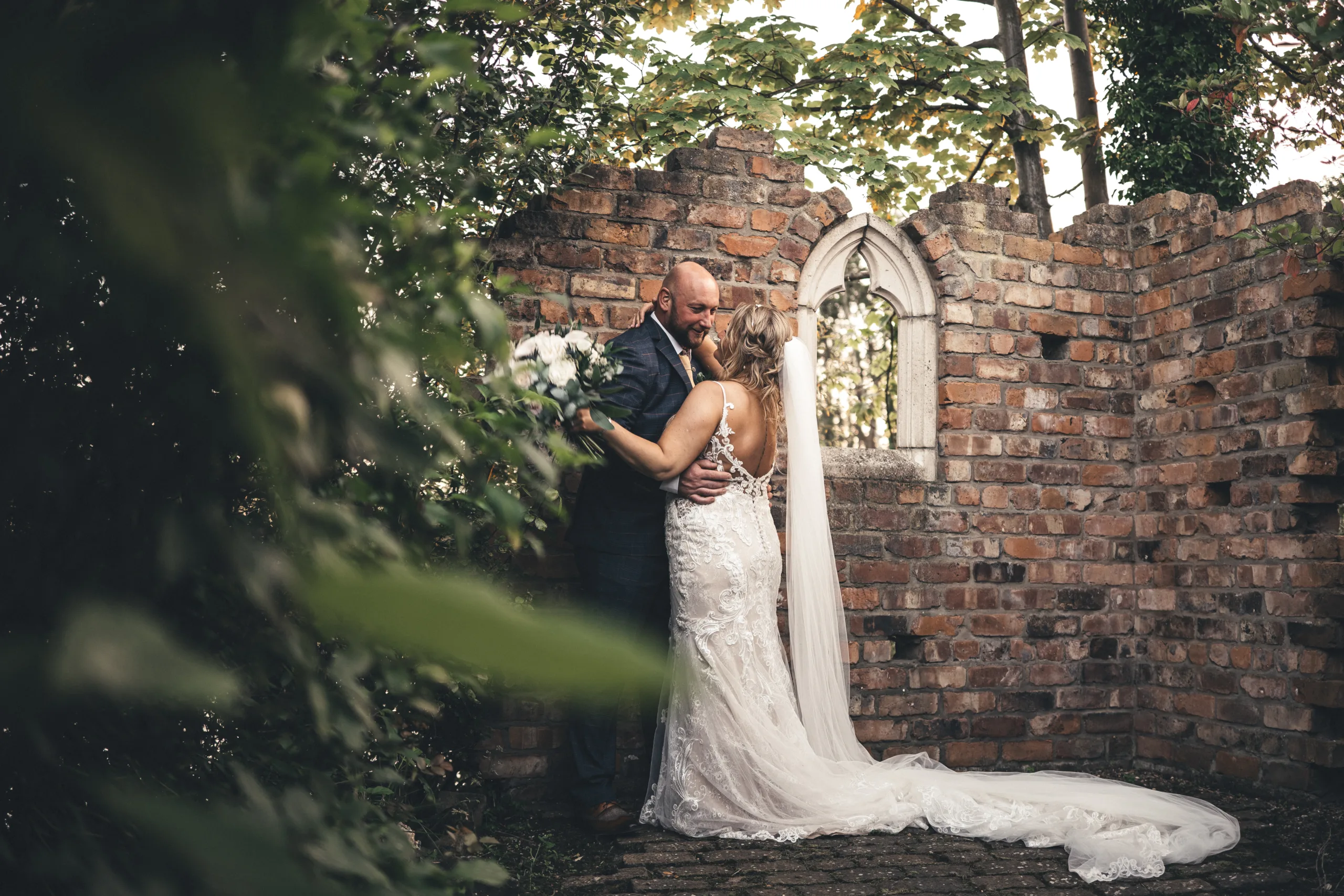 A bride and groom kissing in front of a Yorkshire brick wall.