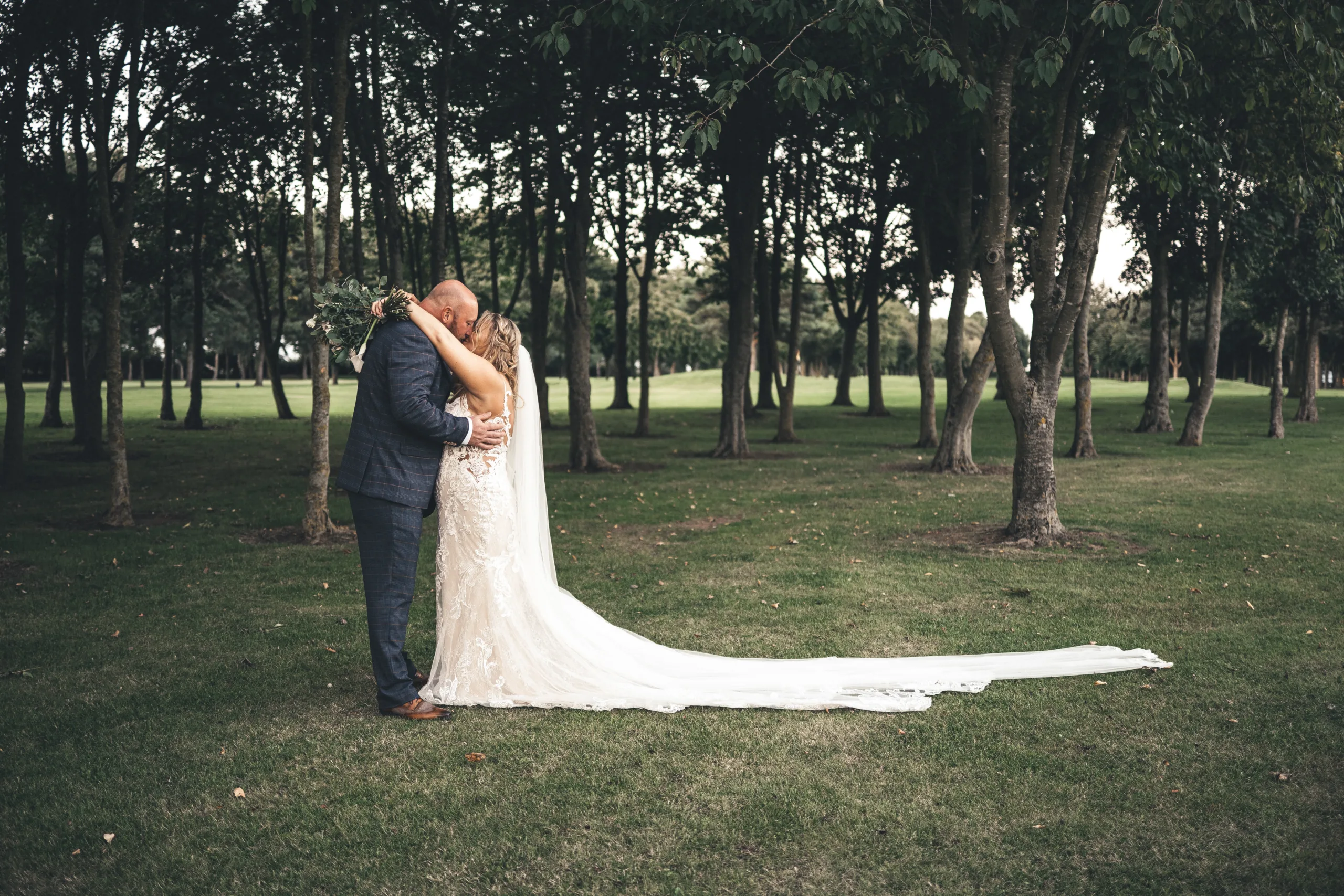 A wedding photographer captures the bride and groom sharing a kiss in a field of trees in Lincolnshire.