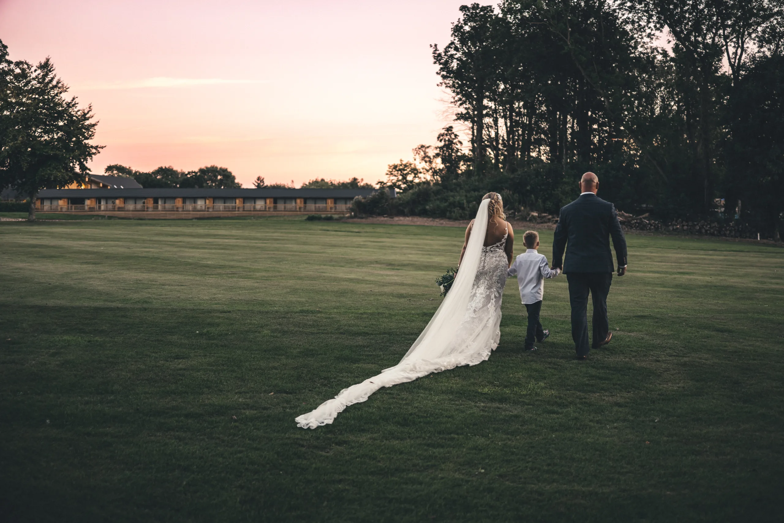 A bride and groom walking in a grassy field at sunset, captured beautifully through Yorkshire photography.