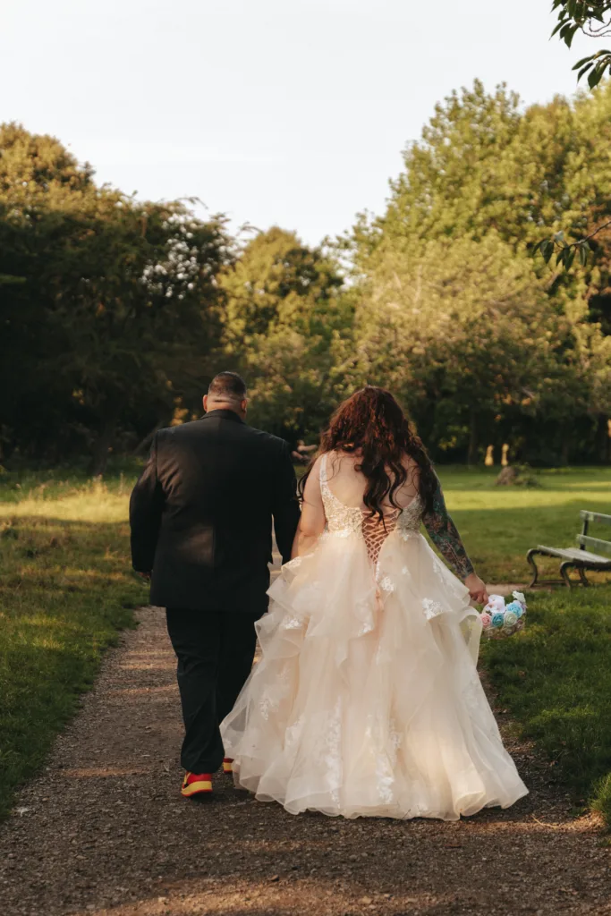 A bride and groom walking down a path in a park, captured by a photographer.