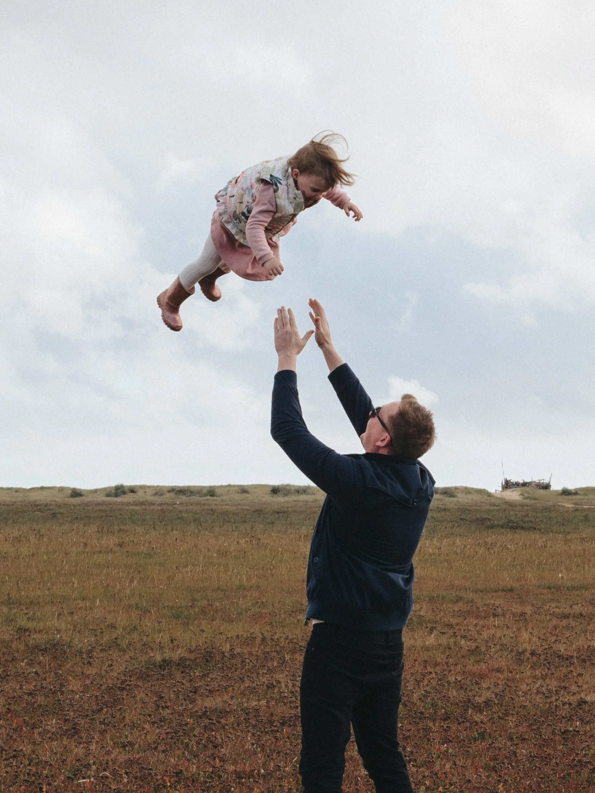 A father and his daughter captured in the air by a photographer in a field.