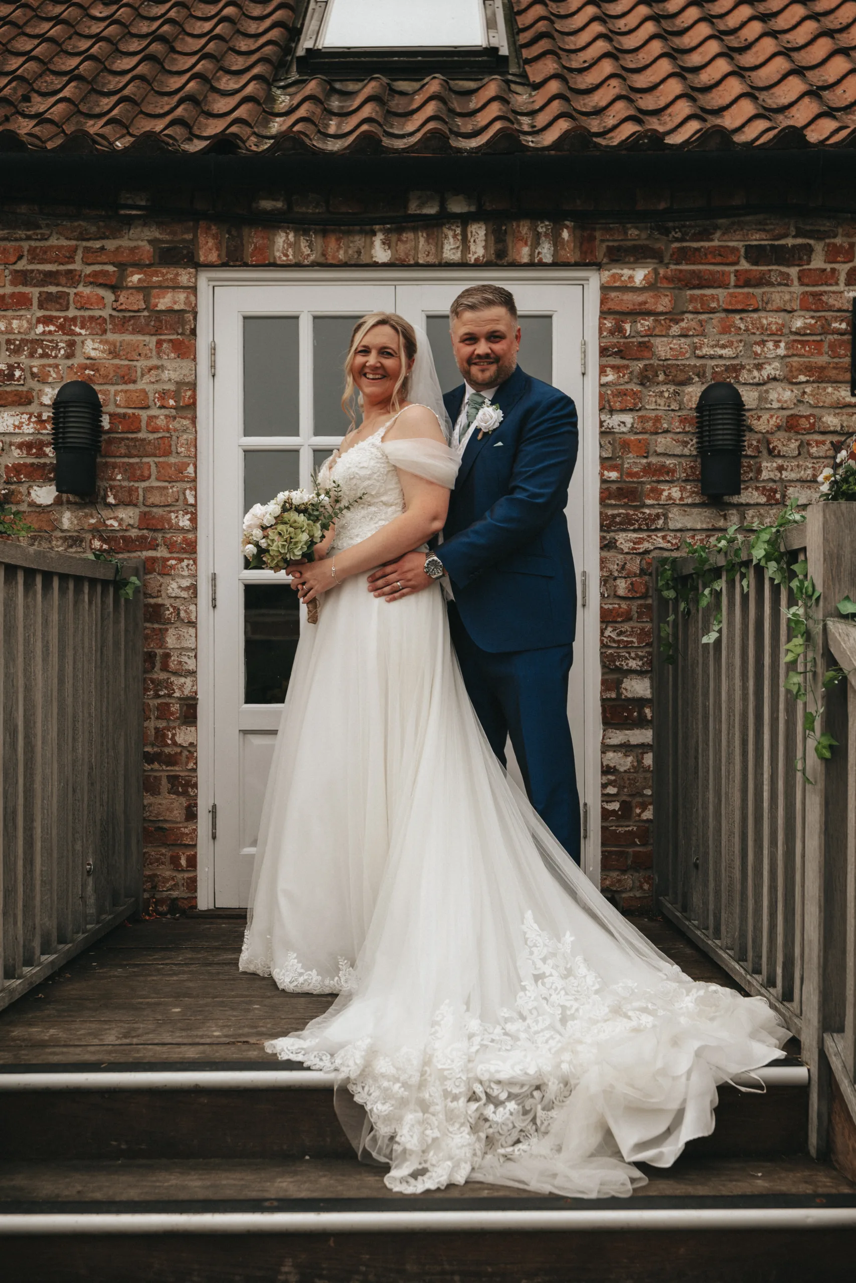 A bride and groom posing in front of a brick house while being photographed by a professional photographer in Lincolnshire.