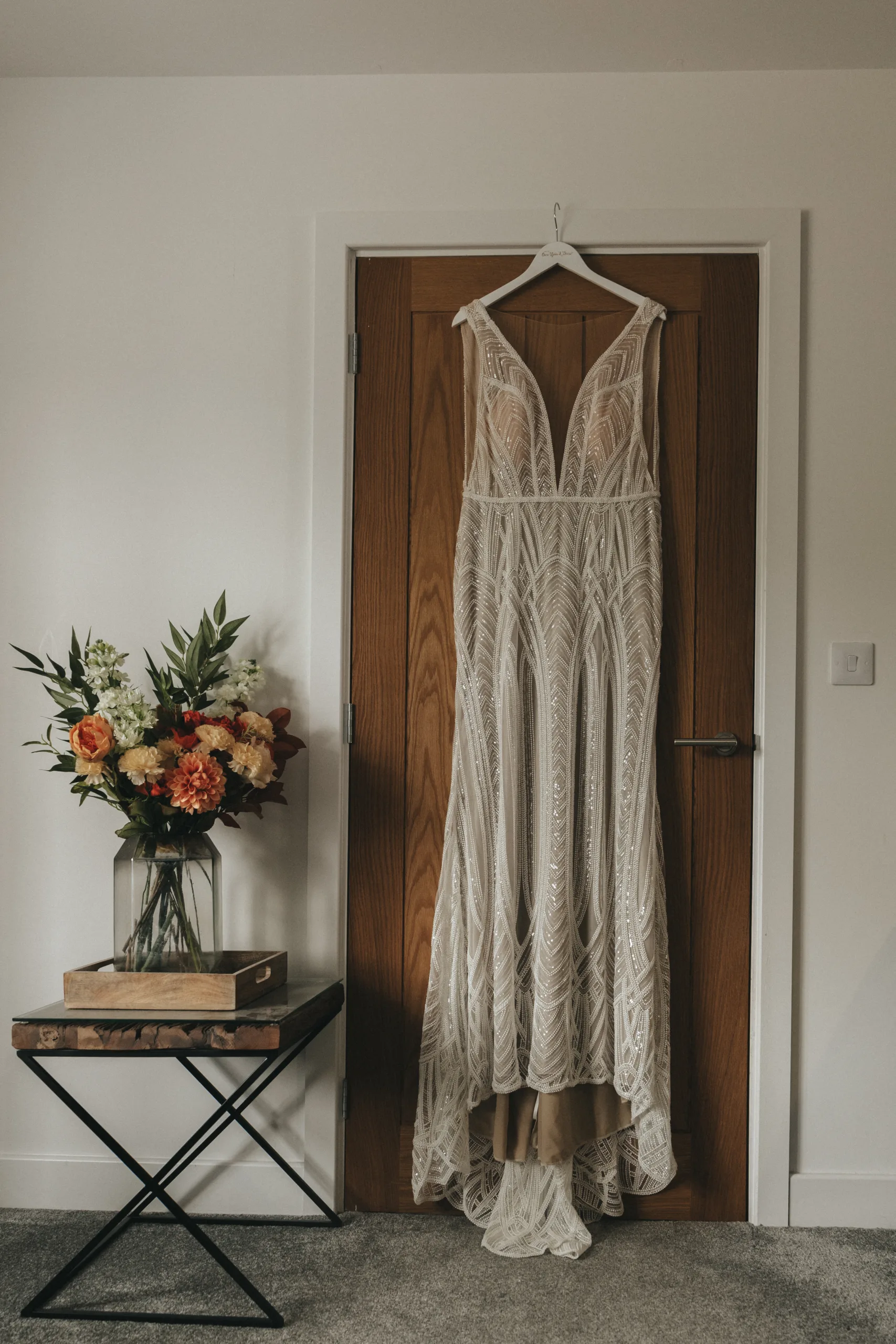 A wedding dress hangs on a door in a room, waiting to be captured by a photographer.