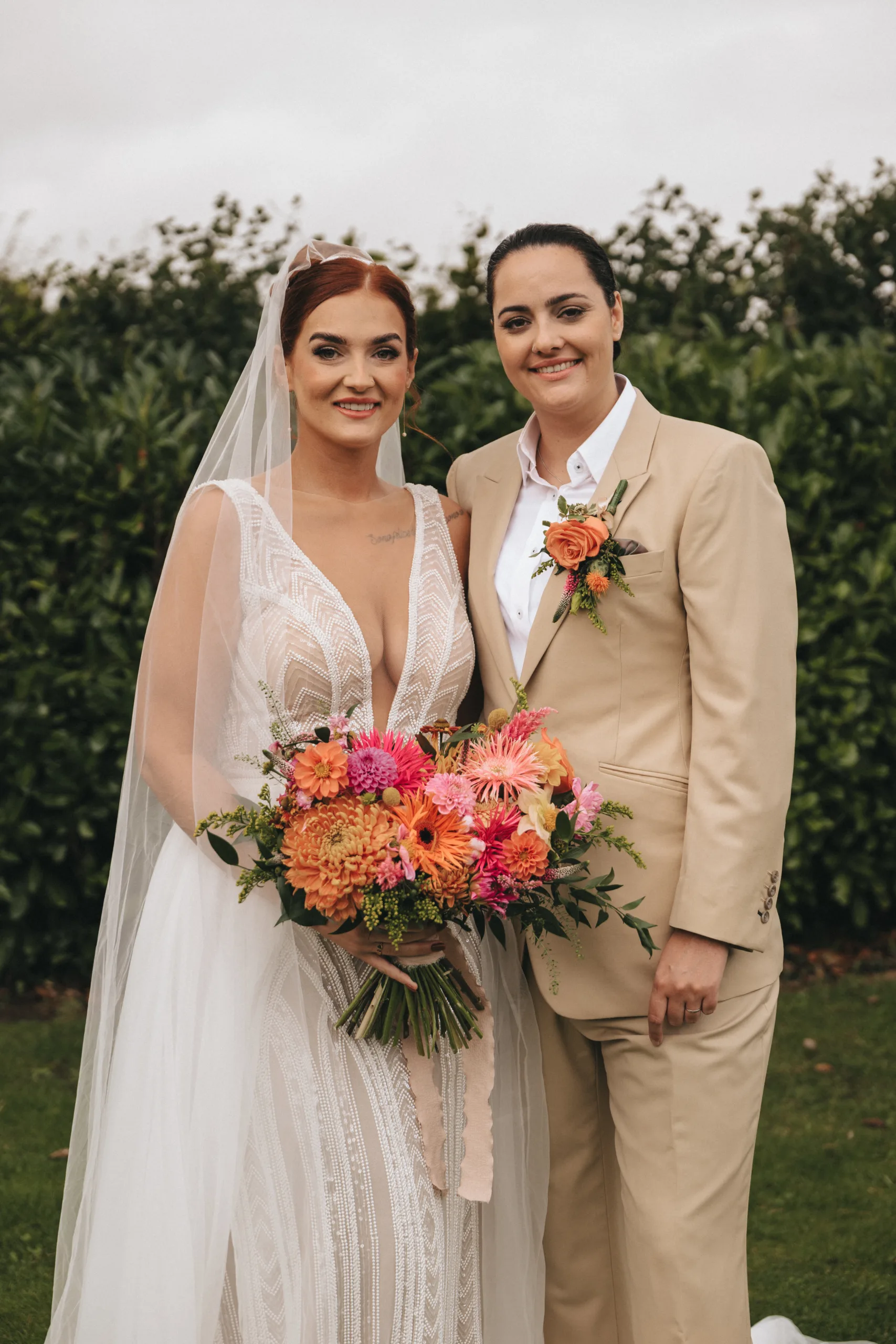 Two brides posing for a wedding photo in a tan suit.