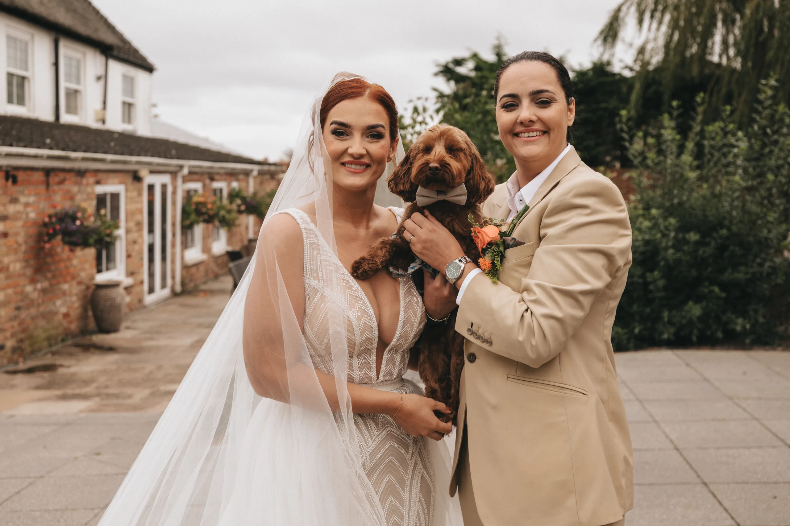 A Yorkshire photographer captures two brides posing with their dog in front of a brick building.