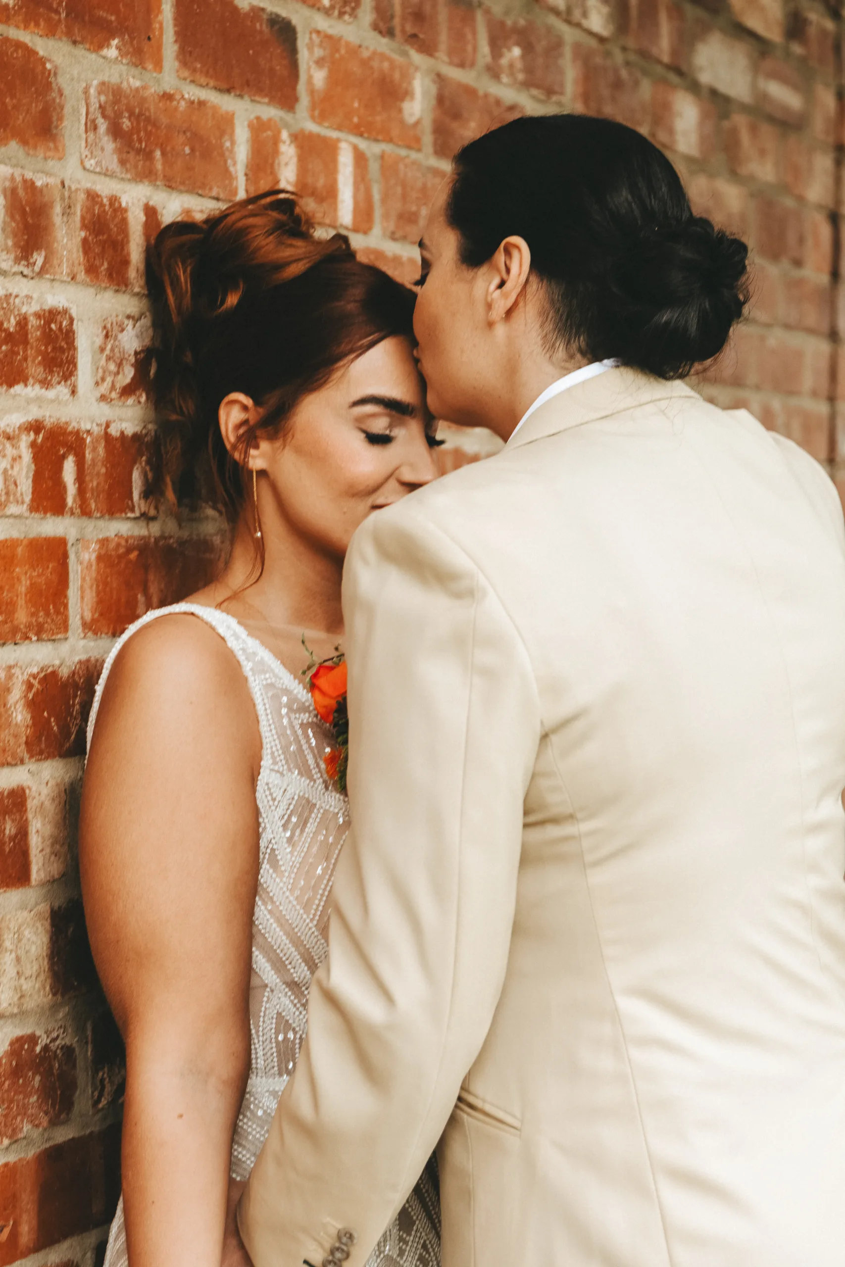 A bride and groom kiss in front of a brick wall during their wedding.