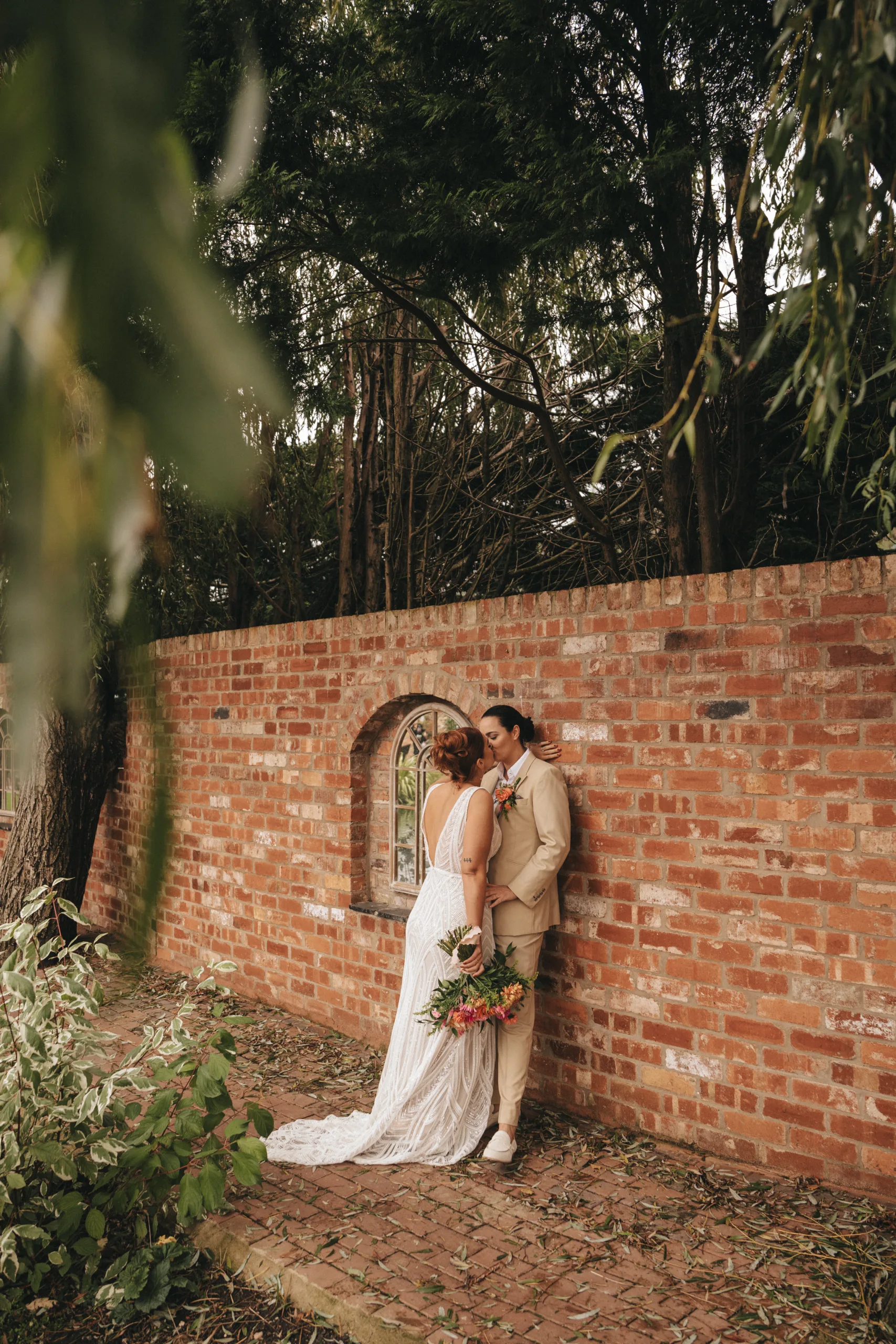 A bride and groom share a kiss in front of a brick wall captured by a wedding photographer in Lincolnshire.