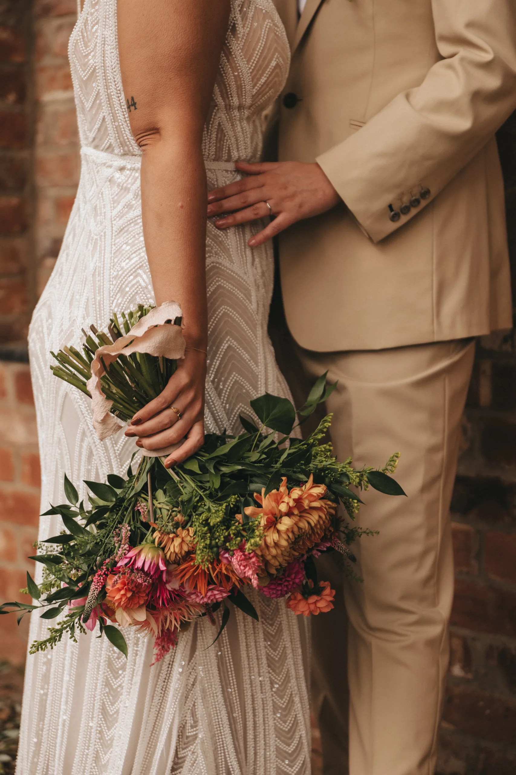 A bride and groom holding a bouquet in front of a brick wall at their Lincolnshire wedding. With photography capturing this special moment.