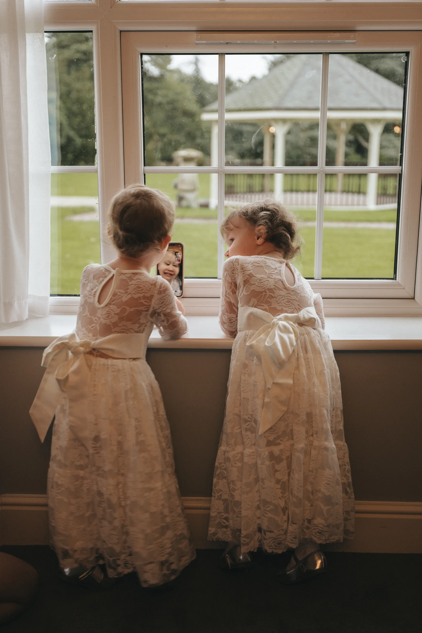 A photographer captures two little girls gazing out of a window in a beautiful moment.