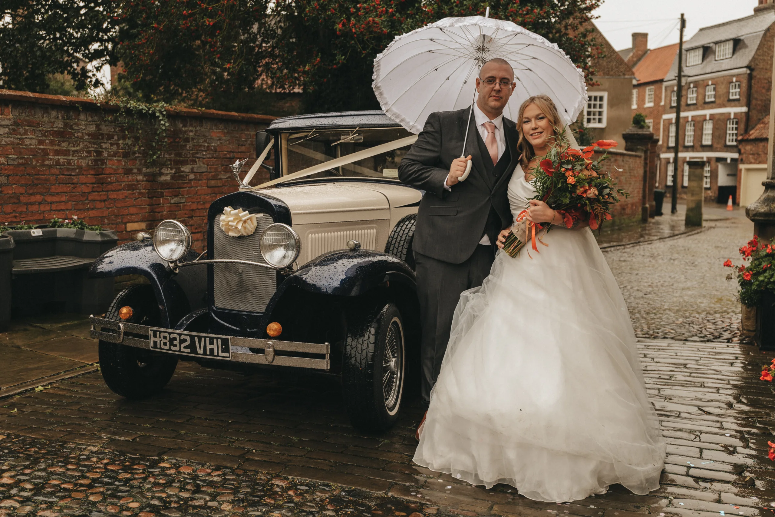 A wedding couple posing in front of an old car for their photographer.