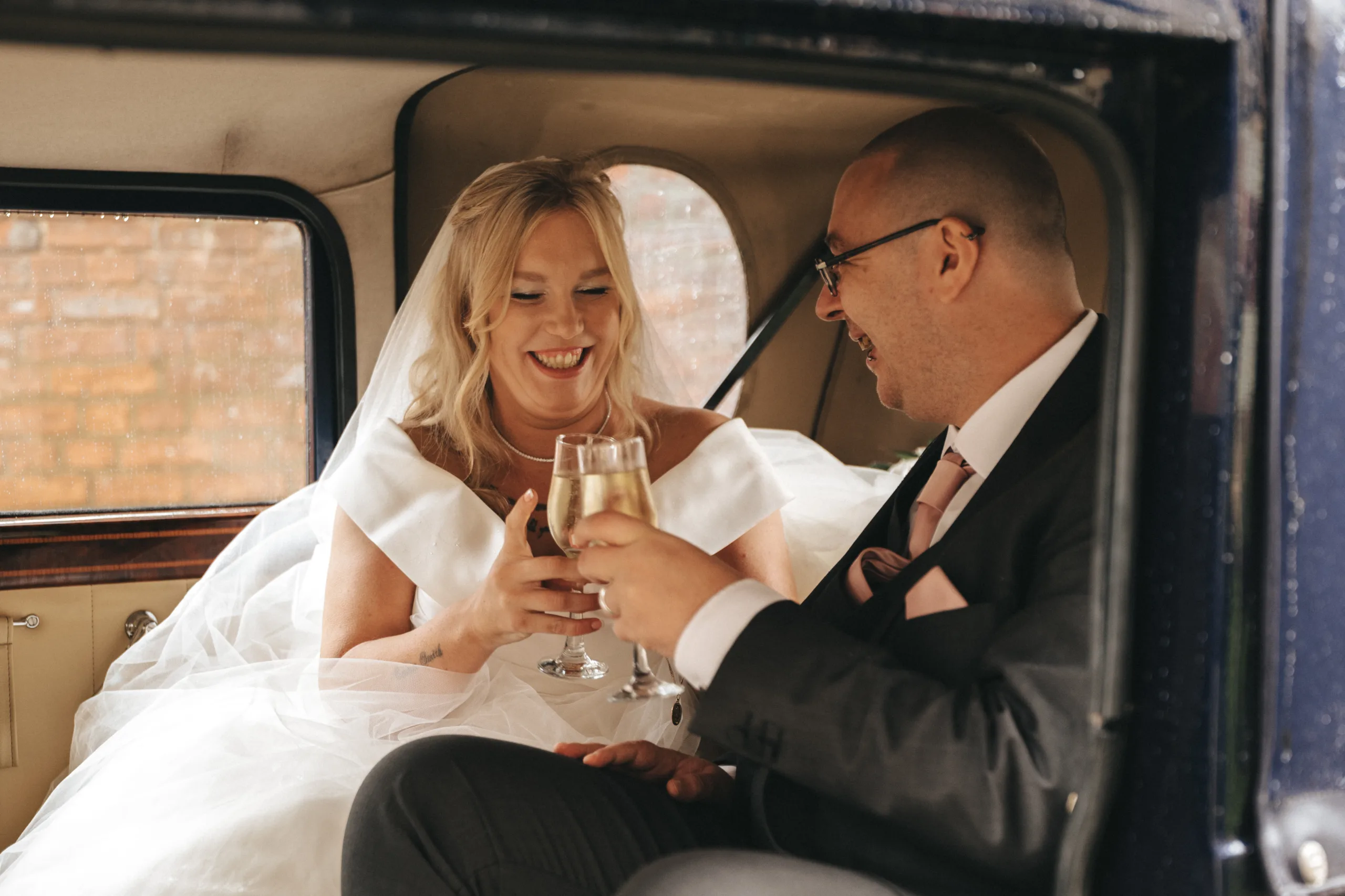 A bride and groom toasting champagne in the back of a vintage car captured by a photographer in Lincolnshire.