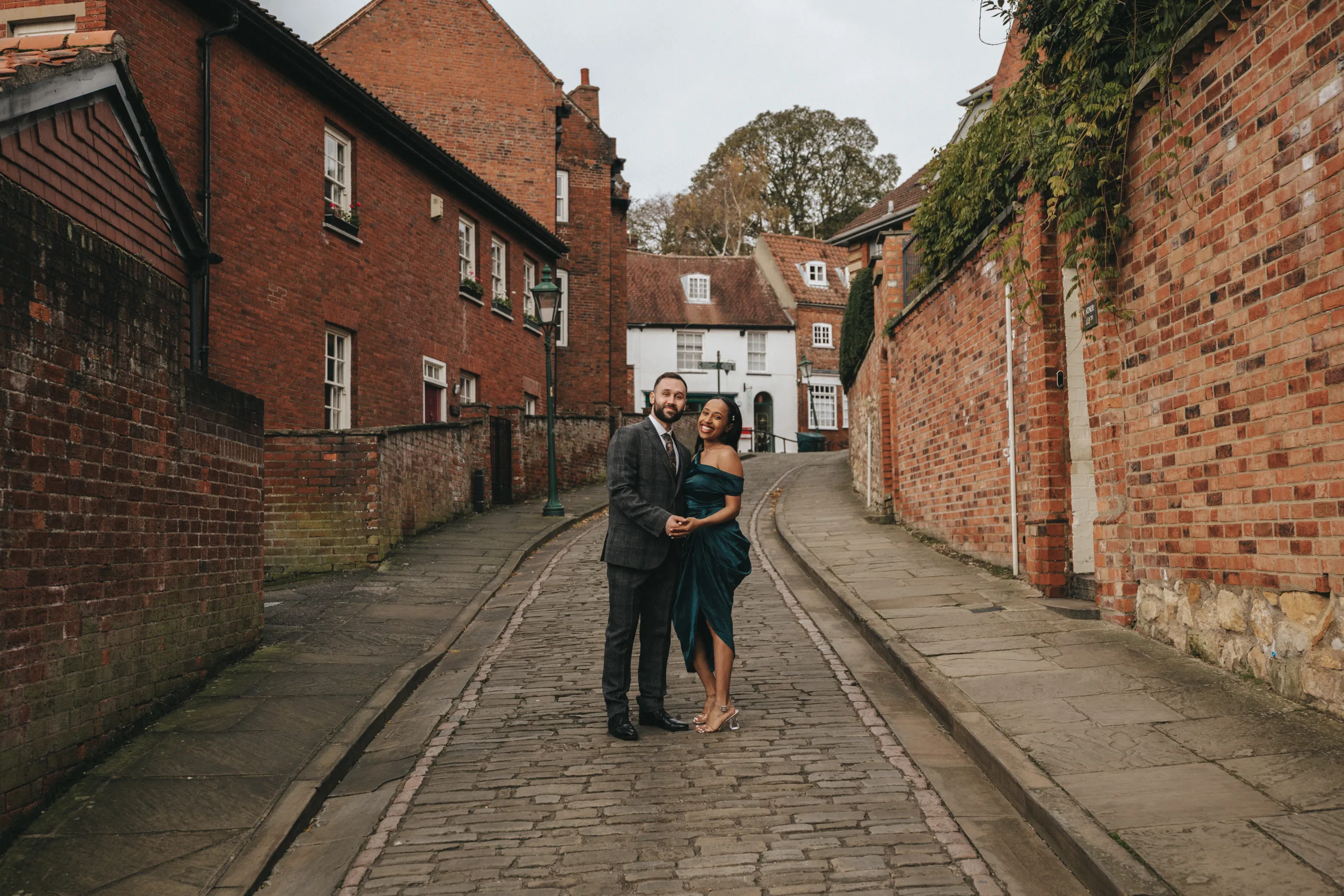 A wedding photographer capturing an engaged couple on a cobblestone street.